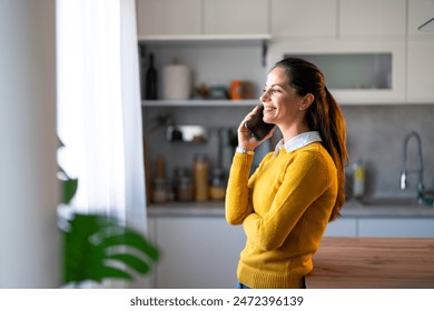 Smiling female entrepreneur discussing over mobile phone while at kitchen counter. - Powered by Shutterstock