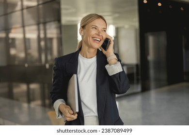 Smiling female entrepreneur is talking phone standing on background of modern office  - Powered by Shutterstock