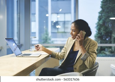 Smiling female executive happy to sign successful contract with company while talking on cellular using laptop computer and wireless connection in office copy space area for your advertising content 