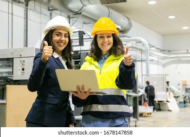 Smiling Female Factory Workers Showing Thumbs Up. Front View Of Cheerful Employees Posing With Laptop At Manufacturing Plant. Print Manufacturing Concept