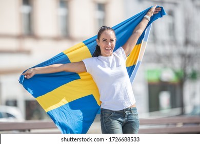 Smiling female fan holds Swedish flag on a street.