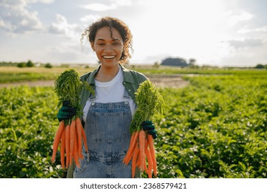 Smiling female farmer holding freshly picked carrots standing in field. Agro industry concept - Powered by Shutterstock