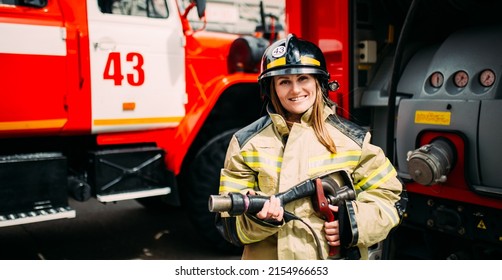 Smiling Female Firefighter In Helmet Looking At Camera Behind At Fire Car.