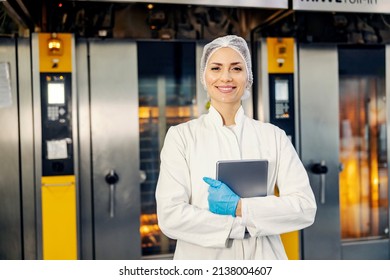 A smiling female food factory inspector with tablet in hands standing in front of ovens in bakery.