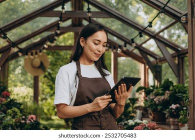 Smiling female gardener standing at greenhouse and looking at digital tablet in hands
 - Powered by Shutterstock