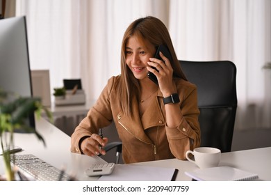 Smiling Female Investment Advisor Consulting Client On Mobile Phone And Using Calculator At Her Office