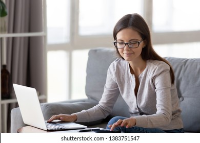 Smiling Female Math Student Sit On Couch Studying On Laptop Doing Research Calculating,  Positive Young Woman Pay Bills Online From Home Make Calculations On Calculator, Check Home Expenses