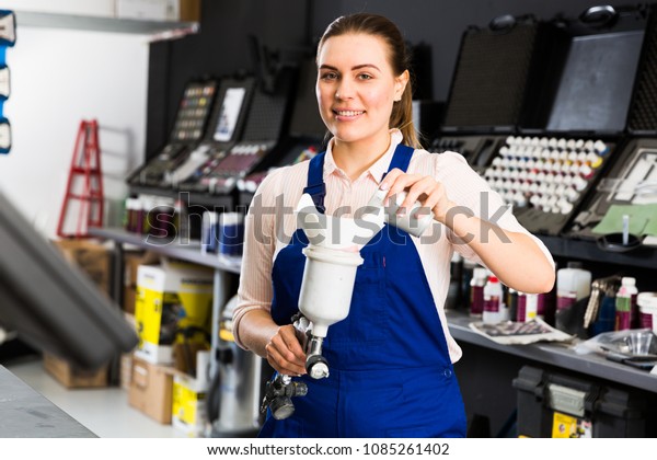 Smiling female mechanic of painting auto workshop\
preparing paint-spray\
gun