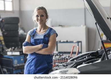 Smiling female mechanic posing next to a car with hood up, women's empowerment concept