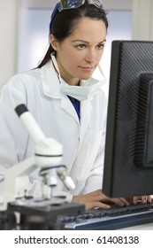A Smiling Female Medical Or Scientific Researcher Or Woman Doctor Using A Computer In A Laboratory With Microscope And Other Equipment In The Foreground.
