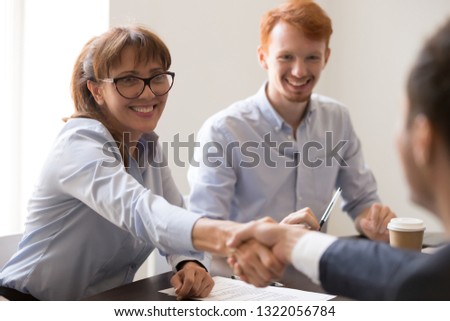Smiling female middle aged hr manager handshaking male applicant making good first impression hiring new worker at job interview, respect, signing contract with client customer at meeting concept