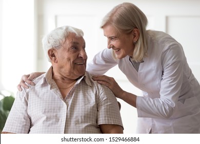 Smiling Female Middle-aged Professional Licensed Practical Nurse Leaned Toward To Elderly Man 80s Clinic Patient People Having Warm Relations Pleasant Conversation, Concept Of Caregiving Care Support