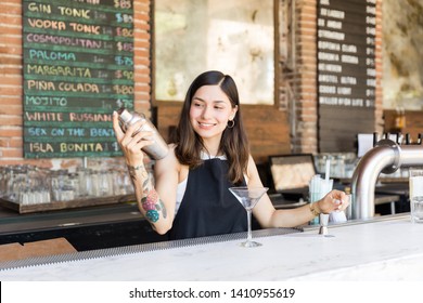 Smiling Female Mixologist Preparing Cocktail In Shaker At Bar Counter