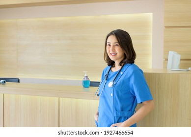 Smiling Female Nurse At A Stacoscope Standing In Front Of A Counter The Back Is An Alcohol Gel.
