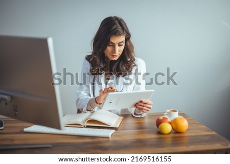 Smiling female nutritionist in her office, writing diet plan showing healthy vegetables and fruits. Healthcare and diet concept. Lifestyle. Online consultation