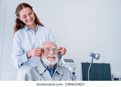 Smiling female oculist helping her mature male patient choose glasses. Optician health checkup. Caucasian female optometrist selecting glasses eye lenses spectacles for senior man - Powered by Shutterstock