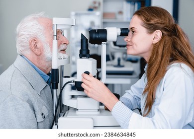 Smiling female ophthalmologist examining mature male patient with the help of ophthalmic equipment. Optician checking eyesight of elderly senior man in clinic hospital - Powered by Shutterstock