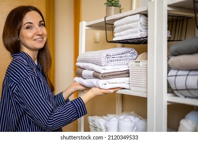 Smiling female in pajamas enjoying homework bedroom minimalist cupboard storage space organizing. Happy housewife making seasonal tidying up putting folded linens use Marie Kondo method at home