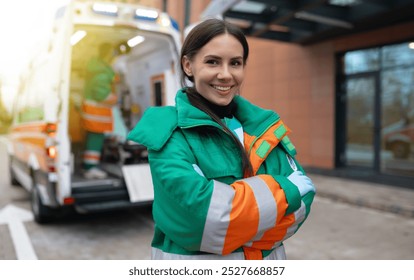 Smiling female paramedic in green and orange uniform stands confidently with arms crossed in front of an ambulance. The image captures professionalism, readiness, and positivity in emergency services - Powered by Shutterstock