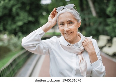 Smiling Female Pensioner Enjoying Sunny Weather While Spending Free Time At Green Park. Attractive Lady With Sunglasses On Head Posing Outdoors.