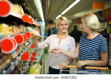 Smiling female pensioner and her adult  daughter choosing chilled sausages in shop