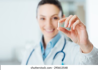 Smiling female pharmacist holding a pill, health care and prevention concept, hand close up