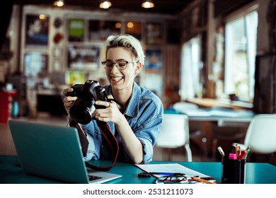 Smiling female photographer reviewing pictures on camera while working on a laptop in creative studio - Powered by Shutterstock