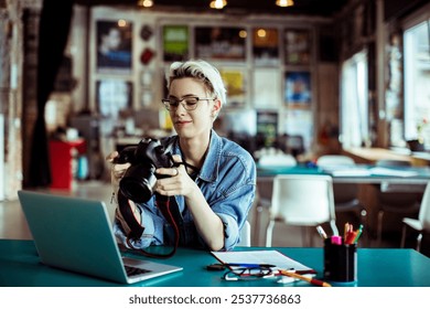 Smiling female photographer reviewing pictures on camera while working on a laptop in creative studio - Powered by Shutterstock