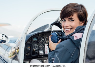 Smiling female pilot in the light aircraft cockpit, she is holding aviator headset and looking at camera - Powered by Shutterstock