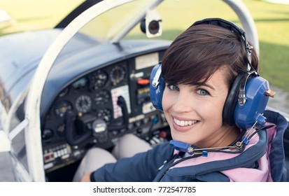 Smiling female pilot in the light aircraft cockpit, she is wearing aviator headset and looking at camera - Powered by Shutterstock