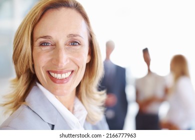 Smiling Female Professional With Associates. Closeup Of Mature Female Professional Smiling With Associates In Background.