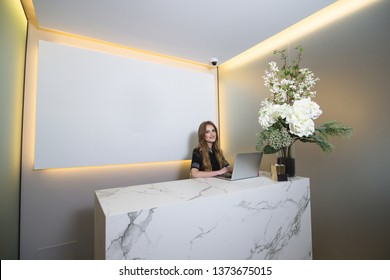 Smiling Female Receptionist Working At The Front Desk In Healthcare Clinic. Mock Up Poster With Copy Space In The Background.