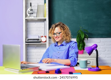 Smiling female school teacher or university professor working with laptop in classroom. Young student girl in glasses preparing for test or exam in college. Learning, education and knowledge concept. - Powered by Shutterstock