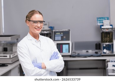 Smiling female scientist crossing arms in modern lab, with analyzers and monitors, copy space. Stainless steel, innovation, research, technology, precision, professionalism, collaboration
