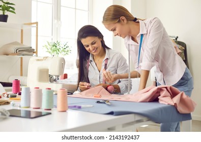 Smiling female seamstress colleagues work together sew clothing in own style workshop. Happy women tailors or designers work in fashion atelier create design garment. Dressmaking concept.