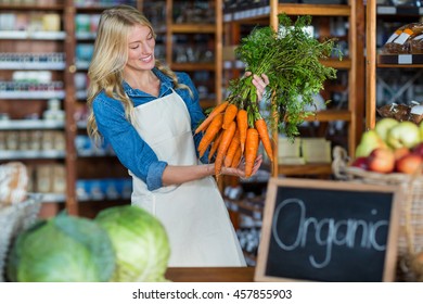 Smiling female staff holding bunch of carrots in organic section of super market - Powered by Shutterstock