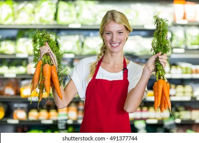 Smiling female staff holding bunch of carrots in organic section - Powered by Shutterstock