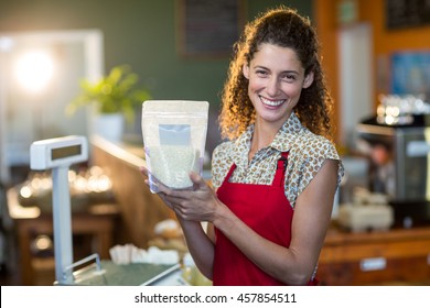 Lächelnde weibliche Mitarbeiter, die an der Zahlungstheke im Supermarkt einen Lebensmittelartikel halten