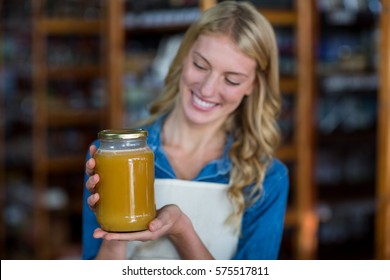 Smiling female staff holding jar of honey in supermarket - Powered by Shutterstock