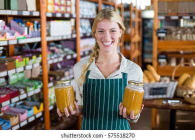 Smiling female staff holding jars of honey in supermarket - Powered by Shutterstock