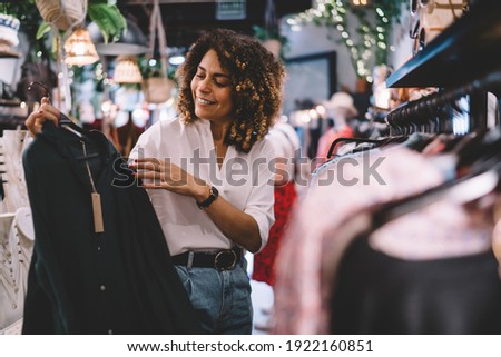 Smiling female standing near hangers with brand wear and laughing during Black Friday shopping with discounts, funny hipster girl enjoying pastime for update her wardrobe spending day in boutique 商業照片 © 
