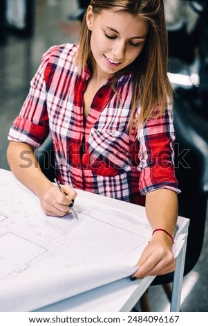 Smiling female student checking coursework blueprint accountings satisfied with great job, positive talented woman architect drawing construction sketch on paper enjoying working process on project