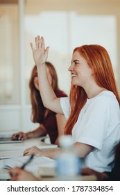 Smiling Female Student Sitting In The Class And Raising Hand Up To Ask Question During Lecture. High School Student Raises Hand And Asks Lecturer A Question.