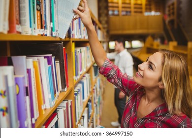 Smiling female student taking book in library - Shutterstock ID 364997150