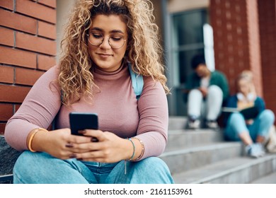 Smiling Female Student Using Mobile Phone While Relaxing On Steps At Campus. 