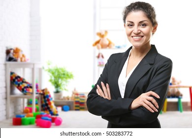 Smiling female teacher with clipboard on blurred playroom background