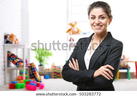 Smiling female teacher with clipboard on blurred playroom background