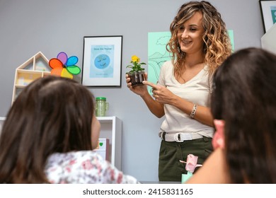 Smiling female teacher showing a pansy plant inside of glass pot to her young students in ecology classroom. Botanical and natural science education concept. - Powered by Shutterstock