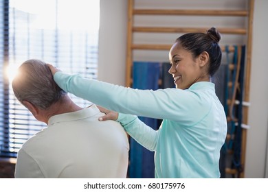 Smiling female therapist examining neck of senior male patient at hospital ward - Powered by Shutterstock