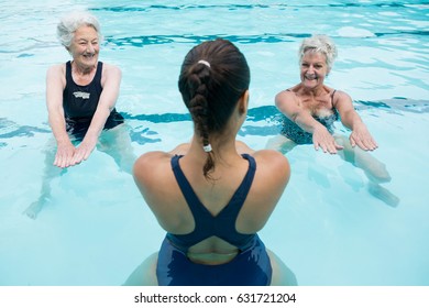 Smiling female trainer with senior women exercising in swimming pool - Powered by Shutterstock